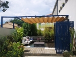 Μπεζ οριζόντια ρωμαϊκή κουρτίνα premium Decor 3x4 σε μεταλλική πέργκολα πάνω από γωνιακό καναπέ κήπου στη βεράντα.
