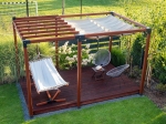 Waterdicht uitschuifbaar schaduwdoek 2,5x3 m gemonteerd op een houten pergola met hangmat en tuinmeubelen.