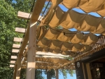 Retractable waterproof shade sail 2.5x3 m mounted on a wooden pergola with decorative festoon lighting.
