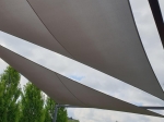 Voile d'ombrage triangulaire grise imperméable premium sur mesure protégeant la terrasse de la pluie et du soleil.