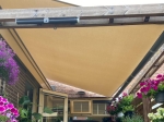 Beige vattentätt premium solsegel 3x2,5 monterat på en träpergola över terrassen med blommor.