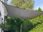 Szürke, méretre szabott HDPE napvitorla, terasz fölé szerelve, zöld kert mellett.