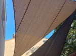 Custom-made triangular HDPE sun sail shade in sand and brown colours installed on a terrace.