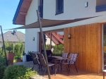 Vela ombreggiante marrone in HDPE 3x3 su una terrazza di una casa moderna con facciata in legno e set di mobili.