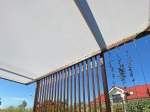 Toldo vela económico blanco a medida, instalado en una estructura de pérgola de madera marrón.