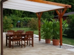 Voile d'ombrage blanche rétractable sur mesure montée sur une pergola en bois au-dessus d'une terrasse avec mobilier.