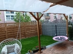 Vela de sombra retrátil branca 2x5 m montada numa pérgula de madeira sobre um terraço com cadeiras suspensas.