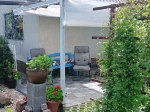 Vela de sombra retrátil branca 3x5 sobre um terraço com banco azul, poltrona confortável e vasos de flores.
