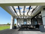 Witte zonwerende lamellen op een modern terras met donkere meubels en een houten pergola.