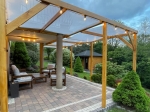 Beige sunshade strip 1x5 m mounted on a wooden pergola over a terrace with garden furniture.