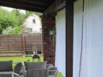 Custom-made voile curtain hanging on a terrace with a garden view and a white house in the background.