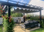 Waterproof horizontal PVC Roman blind mounted on a graphite pergola in a garden with lounge furniture.
