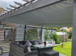 Grey square waterproof custom-made sun shade sail mounted on a wooden pergola over garden furniture.