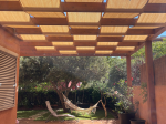 Bande de store banne HDPE sur mesure, montée sur une pergola en bois dans un jardin avec hamac.