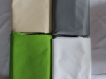 Quatre housses de protection pliées en couleurs beige, gris, vert et blanc, fabriquées sur mesure.