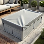 Graue maßgefertigte Schutzhülle für eine rechteckige Gartenbox, auf einer Terrasse neben einem Sofa und Pflanzen platziert.