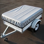 Silver custom-made car trailer tarpaulin, securely fastened and protecting the cargo.