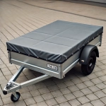 Hopeinen peräkärry mittatilaustyönä tehdyllä harmaalla peitteellä, pysäköitynä kiveykselle.