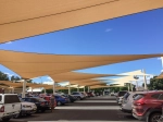 Pânză de umbră triunghiulară bej HDPE 3x3x4,2 suspendată deasupra unei parcări pline de mașini.