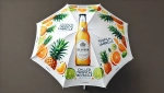 Parasol publicitaire avec motif de fruits tropicaux, inscription « Tropical Umbrella » et illustration d'une boisson en bouteille.