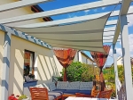 Vierhoekig, waterdicht schaduwdoek op maat gemonteerd op een houten pergola boven een terras met bank.