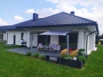 Vela de sombra quadrangular cinzenta impermeável instalada sobre um terraço com mobiliário de jardim moderno.