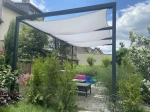 Voile d'ombrage imperméable blanche sur mesure en forme de quadrilatère, montée sur une pergola moderne dans un jardin.