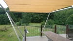 Op maat gemaakt HDPE schaduwdoek vierkant gemonteerd boven een terras met uitzicht op tuin en bos.