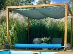Waterproof retractable 3x3 sun sail on a wooden pergola over a pool with a view of ornamental grasses.