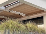 Οριζόντιο premium ρωμαϊκό στόρι Decor 2,5x3 σε μπεζ χρώμα, τοποθετημένο κάτω από στέγαστρο βεράντας πάνω από φυτά.