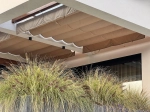 Store romain horizontal premium Decor 2,5x3 de couleur beige, installé sous un toit de terrasse au-dessus de plantes.