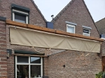 Store romain horizontal premium Decor 2,5x3 m en beige, monté sur une poutre de terrasse en bois.