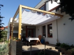 Ανοιχτόχρωμο οριζόντιο ρωμαϊκό στόρι premium Decor 3x4 τοποθετημένο σε ξύλινη πέργκολα πάνω από τη βεράντα με έπιπλα κήπου.