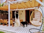 Οριζόντια ρωμαϊκή ρολέτα premium Decor 3x4 πάνω από βεράντα με σκύλο, κρεμαστή πολυθρόνα και ξύλινα έπιπλα κήπου.
