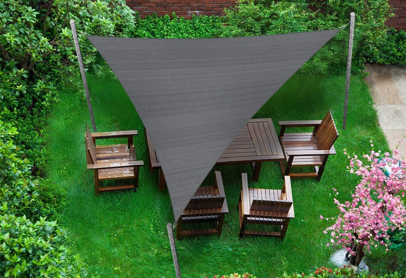 Çim alan üzerindeki ahşap bahçe mobilyalarının üzerine monte edilmiş gri üçgen HDPE güneş yelkeni 4,2x4,2x5,9 m.