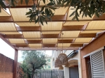 Fascia per gazebo chiara in HDPE 0,4x5m intrecciata tra le travi di una pergola in legno sulla terrazza, per fare ombra.