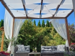 Måttbeställt vitt solskydd monterat på en träpergola med grå trädgårdsmöbler.