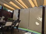Cortina para cenador Premium en color beige instalada en una terraza de madera con muebles de jardín y toldo romano.