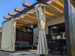 Cortina de cenador Premium en color beige montada en una pérgola de madera con muebles de jardín.