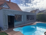 Fermeture de terrasse grise transparente sur mesure avec fenêtres PVC, installée près d'une piscine sur une terrasse en bois.