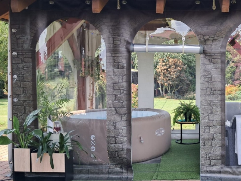 Personlig terrassepresenning med steinvegg-grafikk og vinduer som skjermer avslapningssonen med Lay-Z-Spa jacuzzi.