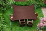 Custom-made brown HDPE shade sail shading wooden garden furniture set on a lawn.
