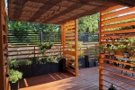 Horisontell romersk rullgardin av HDPE-material monterad efter mått under en träpergola på en terrass med växter.