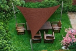 Custom-made brown triangular HDPE sun sail shading wooden garden furniture on a lawn.