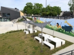 Šedá trojúhelníková sluneční clona HDPE na míru zastiňující odpočinkové stolky na moderním hřišti.