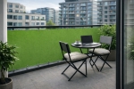 Green waterproof custom-made balcony screen mounted on the railing of a modern terrace with garden furniture.
