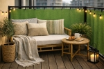 Custom green waterproof balcony privacy screen mounted on the railing of a cozy balcony with garden furniture.