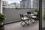 Sivá vodotesná balkónová clona na mieru namontovaná na zábradlí moderného balkóna so stolíkom a stoličkami.