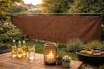 Custom-made brown HDPE fence screening mounted on a fence in a sunny garden with a barbecue and terrace.