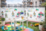 Kleurrijk balkonzeil op maat met circusmotief, speelhoek voor kinderen met witte tafel en matten.